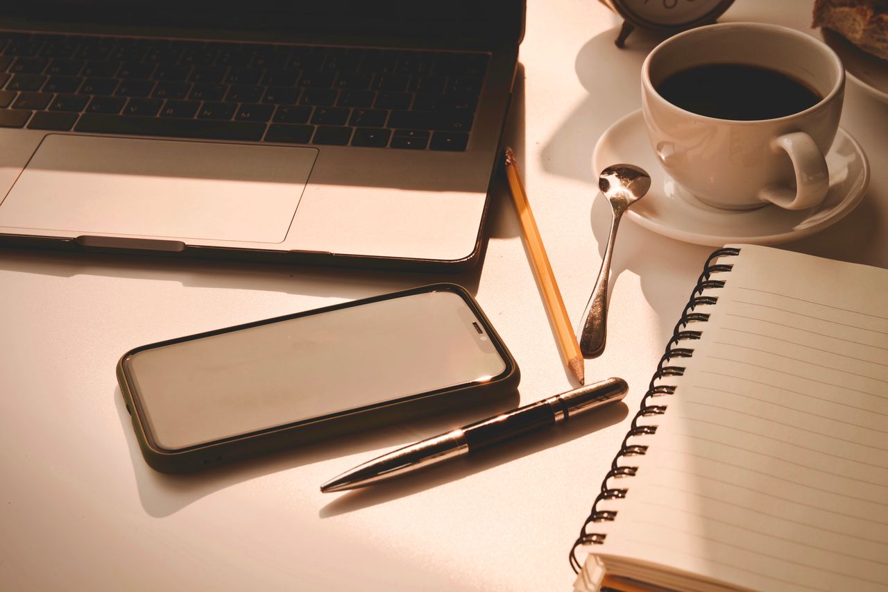 A laptop and notebook on a table in the early morning light